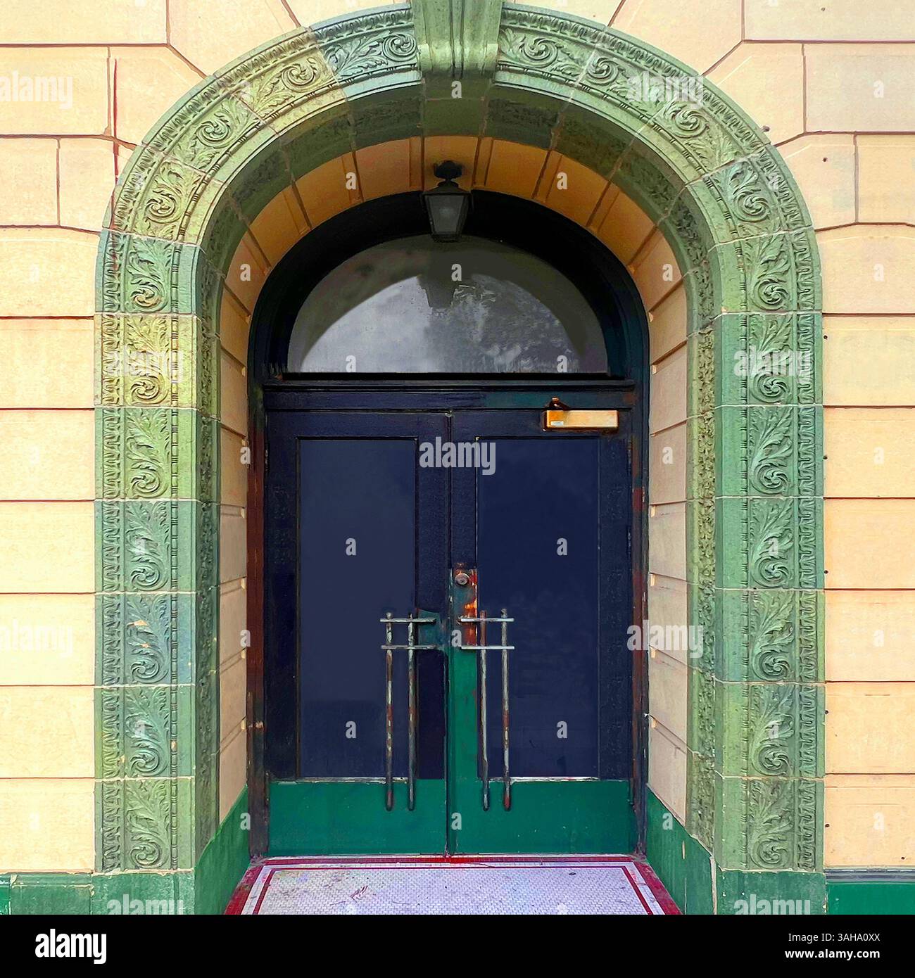 Elegant double doors framed by an arched green terracotta portal with ornate foliate detailing, set in a yellow stone building in Chicago - Smartphone Captured Stock Image