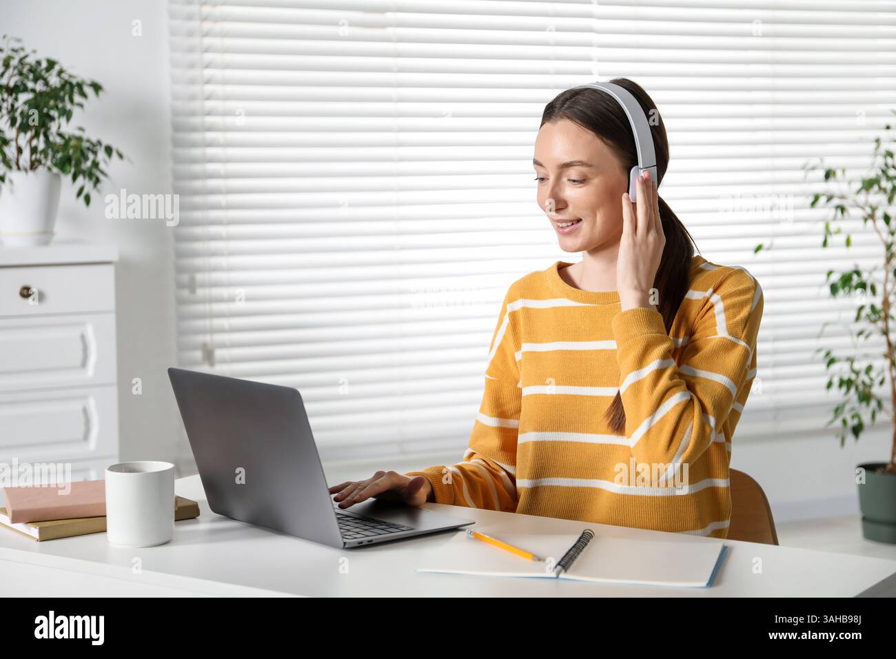 Smiling woman learning online using laptop at table indoors. Self-study Stock Photo