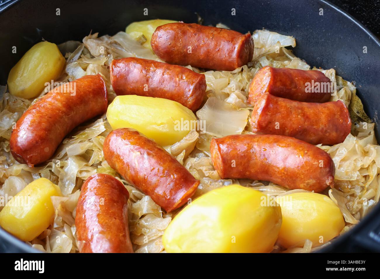 Authentic and hearty dish featuring savory sausages, whole potatoes, and cooked cabbage, prepared together in a pan for a satisfying meal. Stock Photo