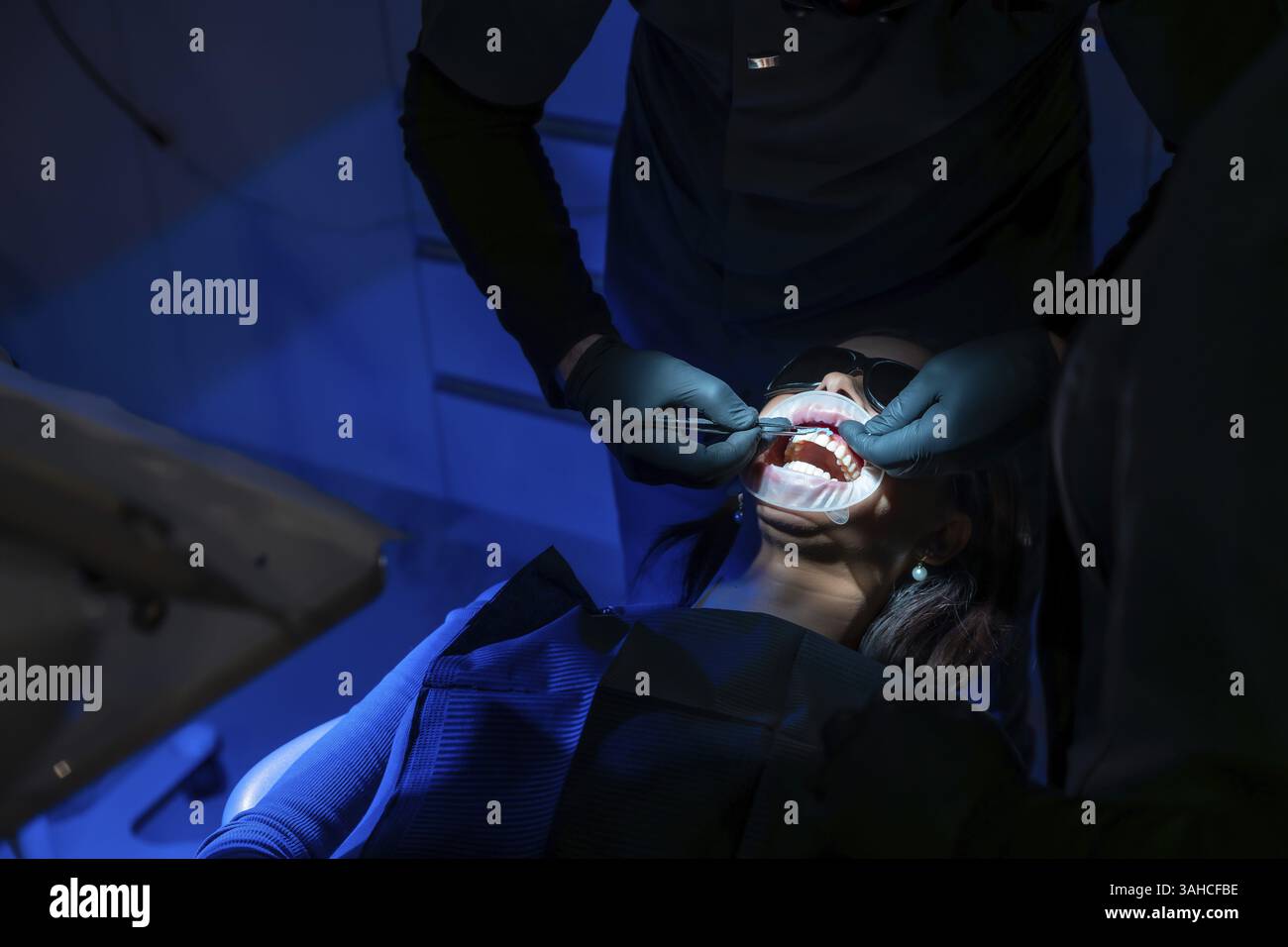 A dentist in a dental clinic applying whitening gel to patient's teeth
