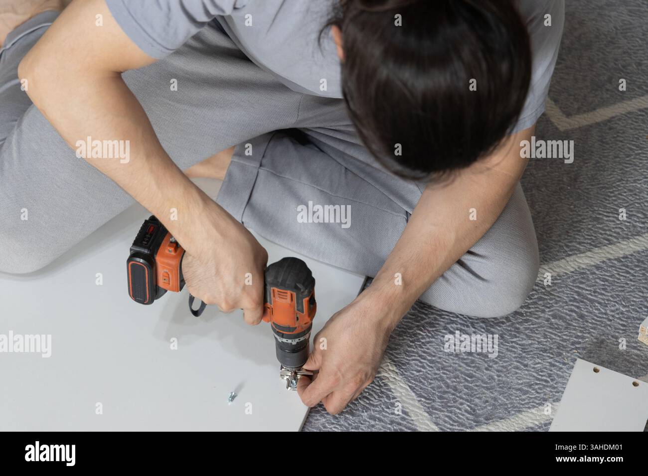 Man assembling wardrobe at home using power drill. Stock Photo