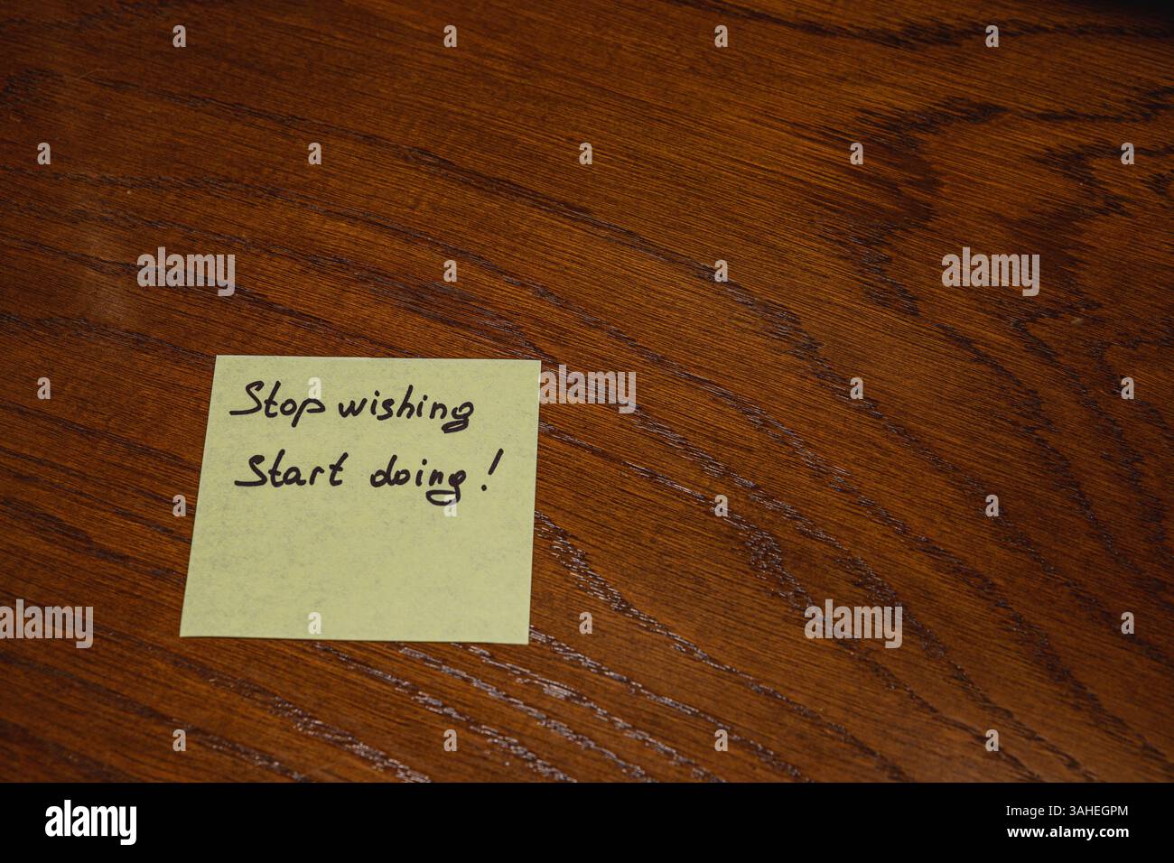 A yellow sticky note rests on a wooden table with a motivational ...