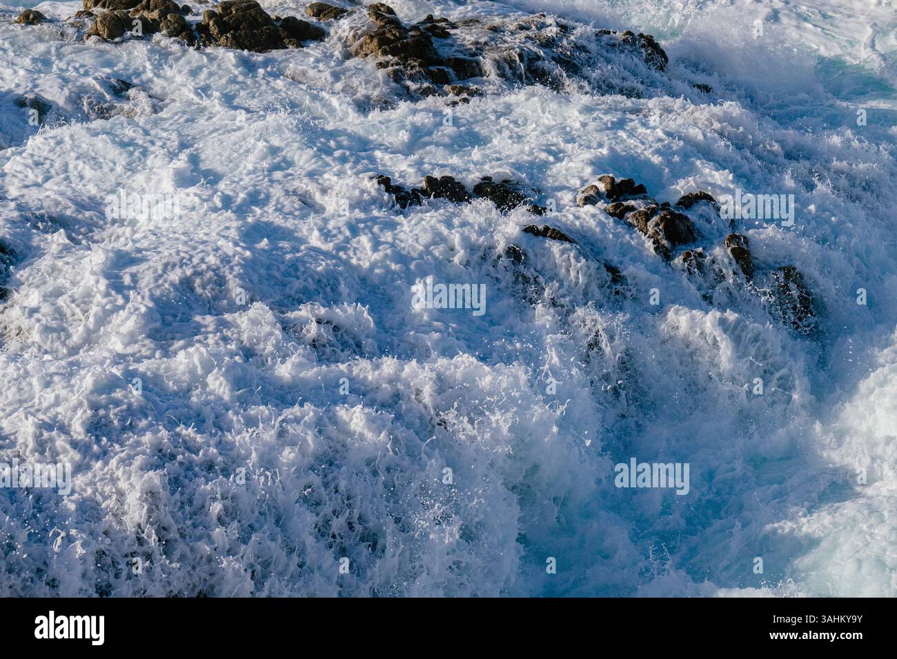 Ocean waves crash powerfully against rocky shore, creating white foam and dynamic motion. Monterey, CA, USA Stock Photo