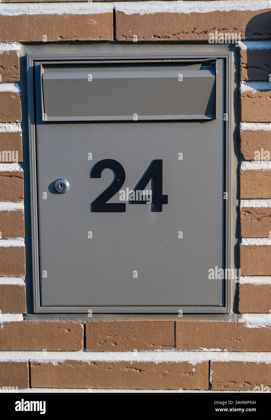 A modern gray mailbox with the number 24 is embedded in a brick wall ...