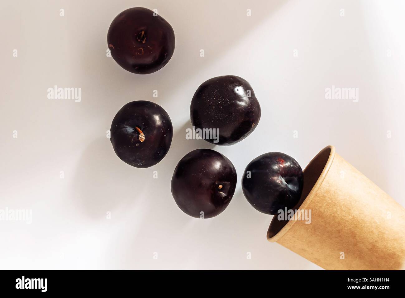 Bunch of black plums are in a brown paper cup. The cup is half full and ...