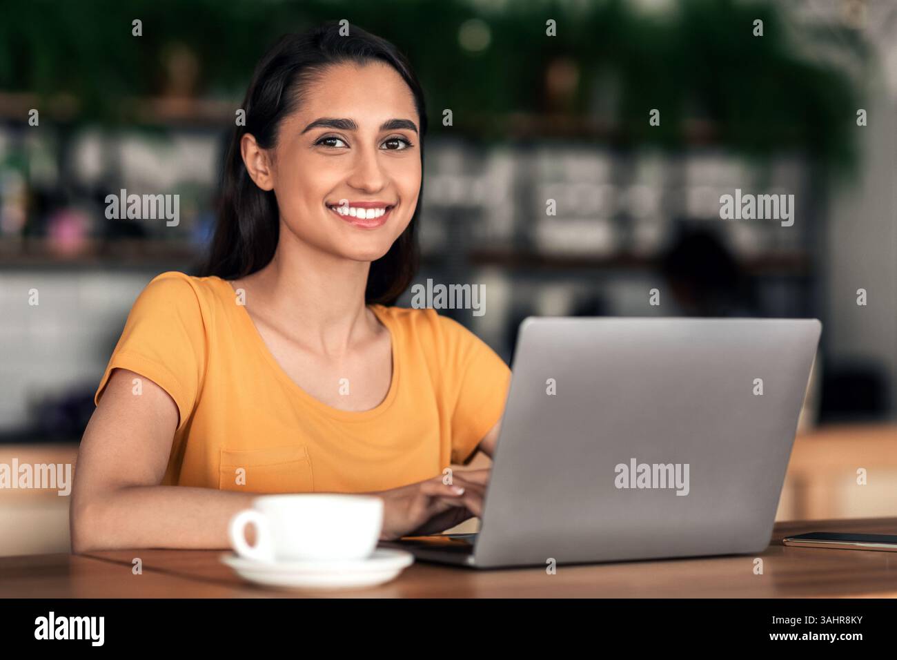 Cheerful female student using laptop at cafe Stock Photo
