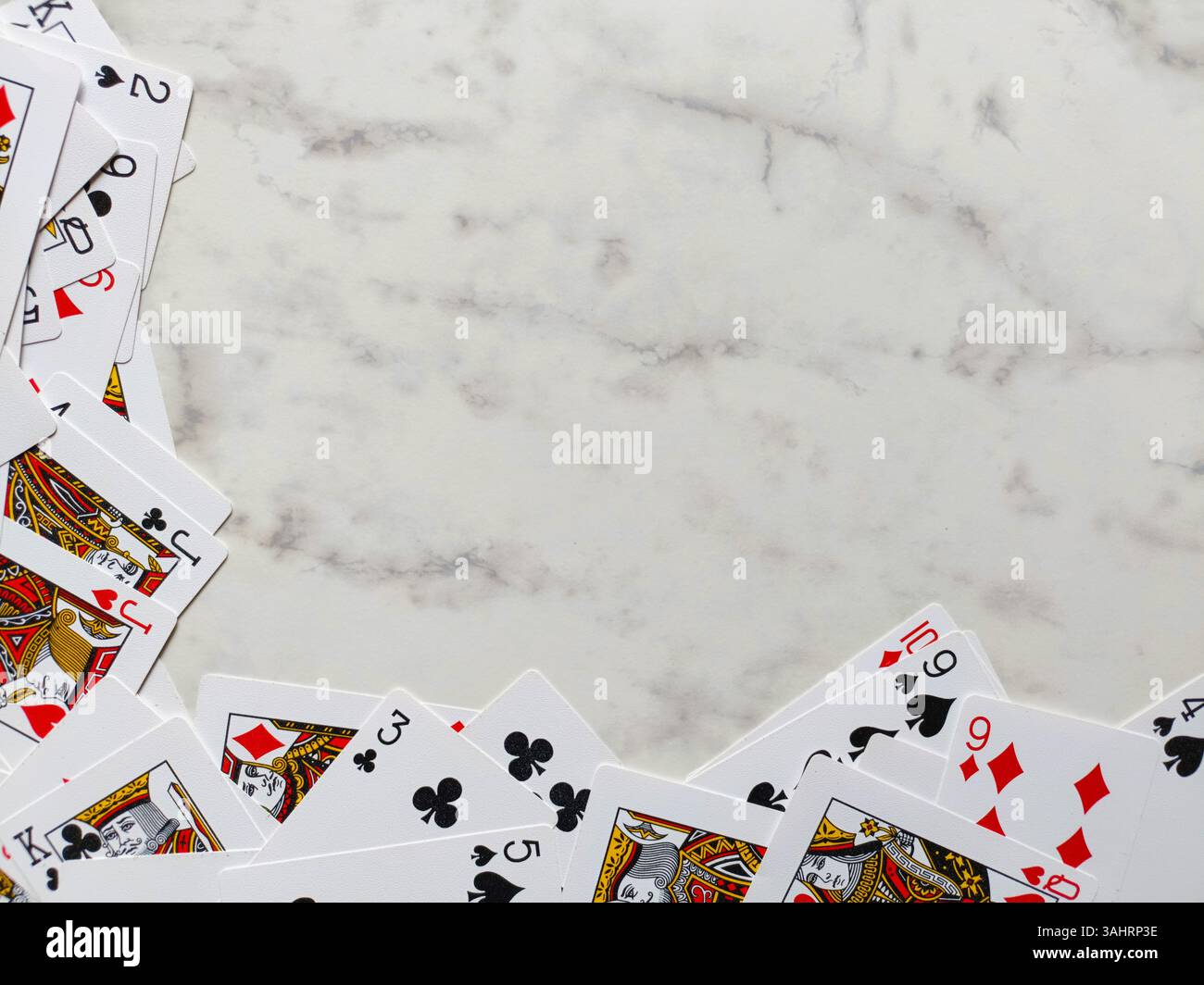 scattered arrangement of playing cards on a white marble surface. The cards are primarily positioned around the bottom and left edges of the frame - Smartphone Captured Stock Image
