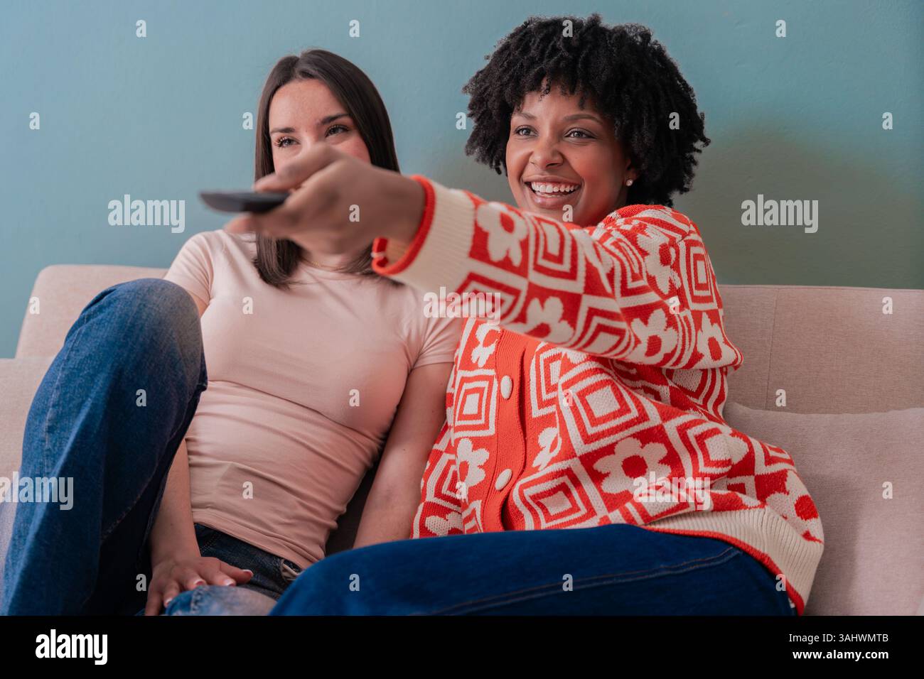 Two diverse women smiling on sofa watching TV together, enjoying