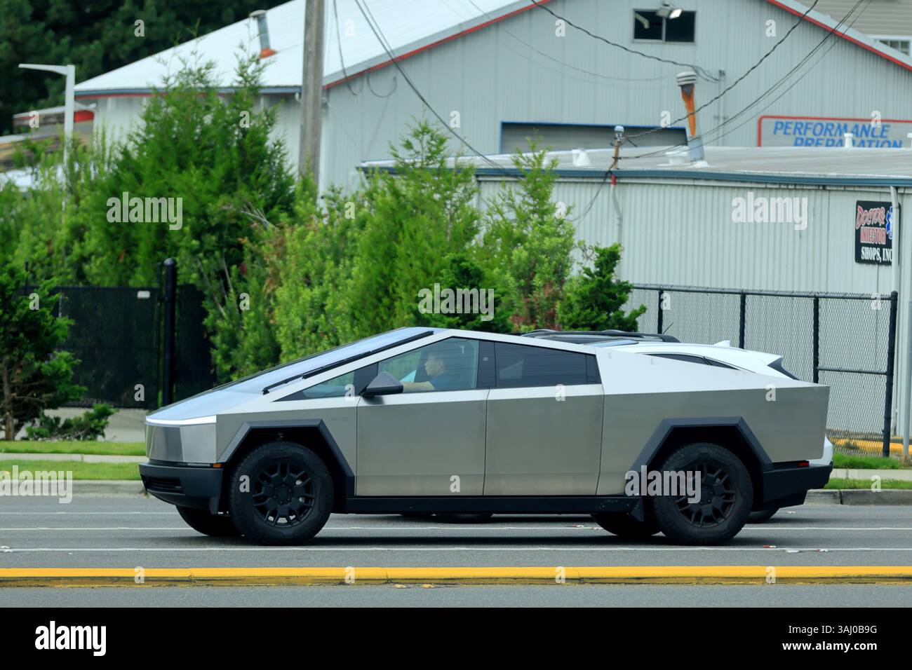 A Tesla Cybertruck with its distinctive angular design and stainless steel body drives on a road in Seattle, Washington, near a building Stock Photo