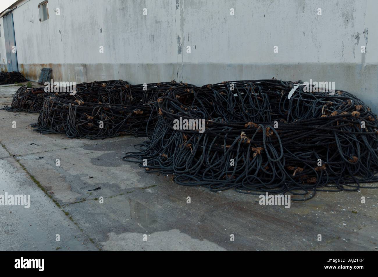 Old, worn fishing nets are piled up on the ground near a coastal warehouse, suggesting recent fishing activities or equipment storage Stock Photo