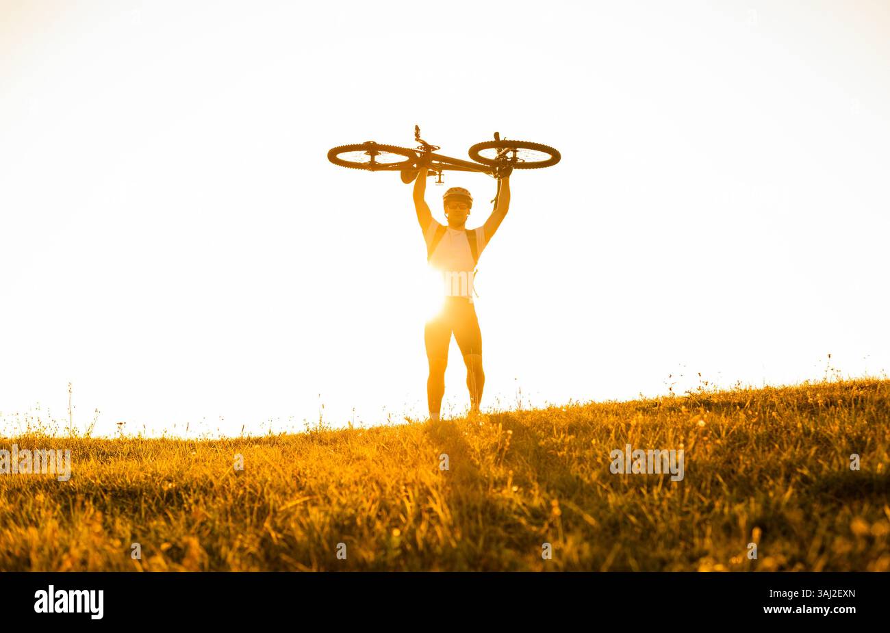 Happy man cyclist celebrating victory holding his bicycle over himself on sunlight background concept of a sports success victory. Stock Photo