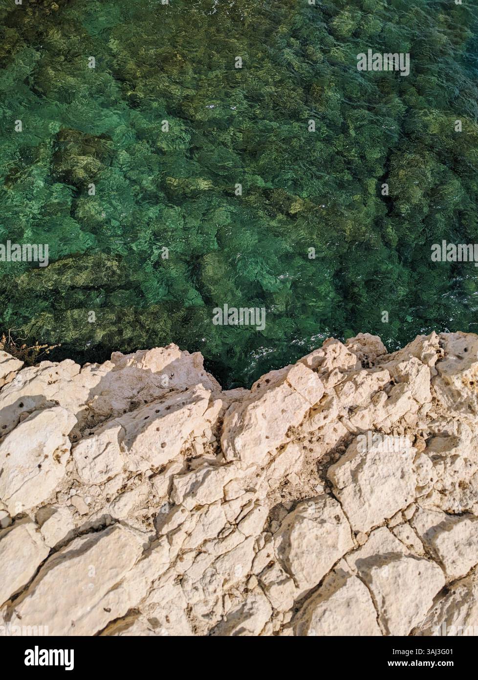 From the edge of Ektoras Beach, Cyprus limestone cliffs overlook crystal-clear waters teeming with life and layered in emerald tones. - Smartphone Captured Stock Image From the edge of Ektoras Beach, Cyprus limestone cliffs overlook crystal-clear waters teeming with life and layered in emerald tones. - Smartphone Captured Stock Image