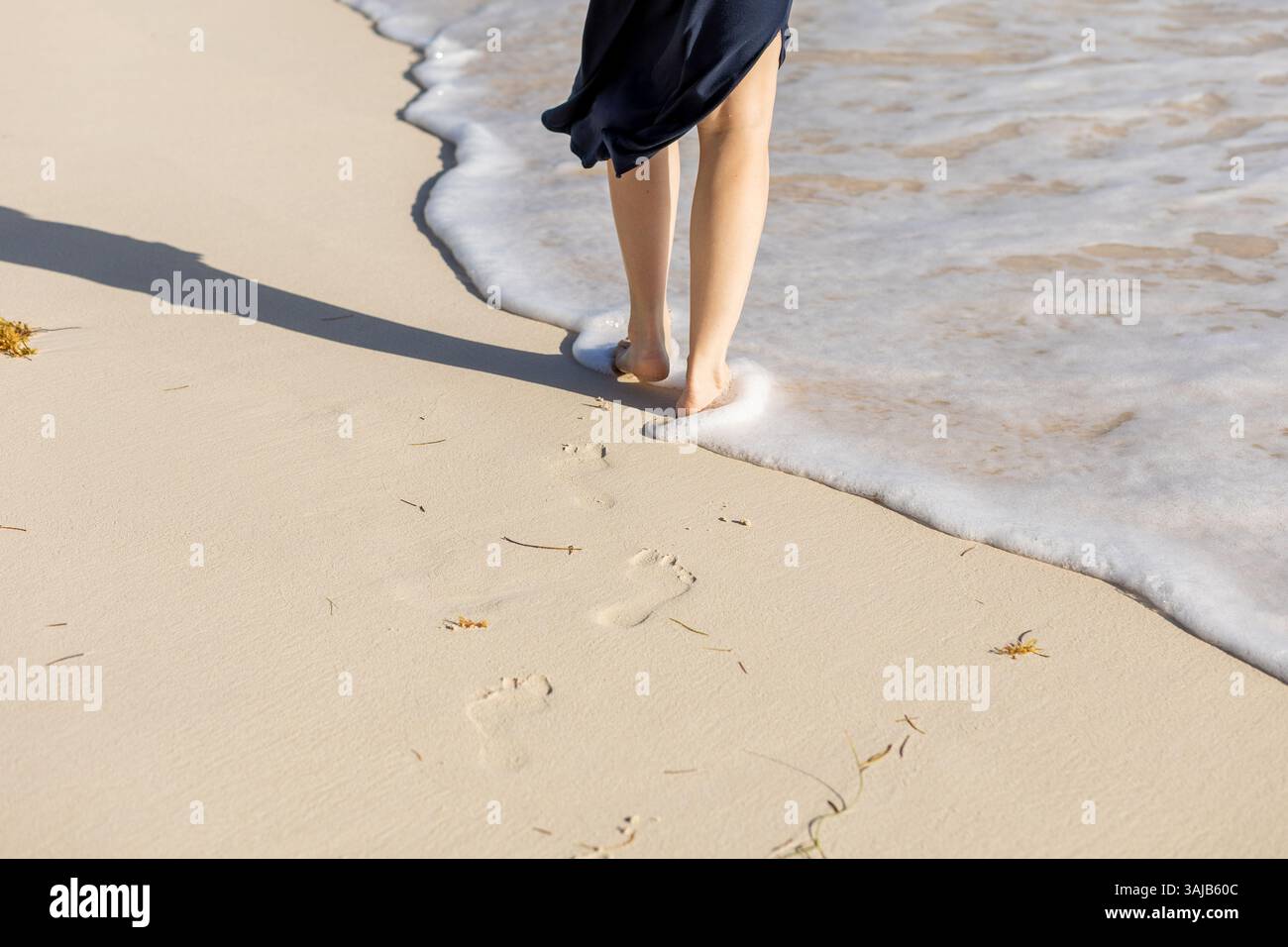 A person walks barefoot along the beach, leaving footprints in the soft ...