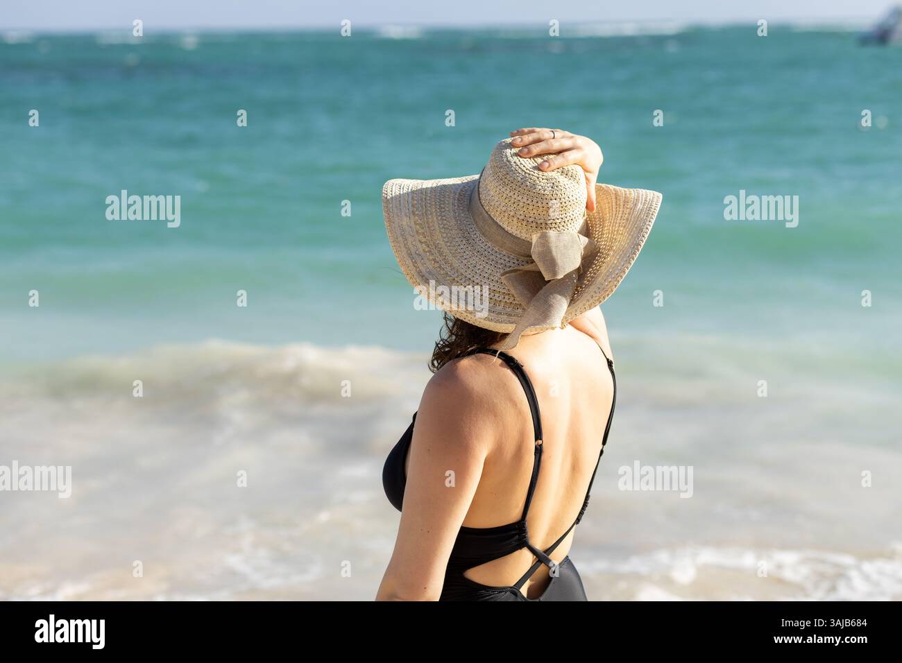 On a bright day at the beach, a young woman stands with her back to the ...
