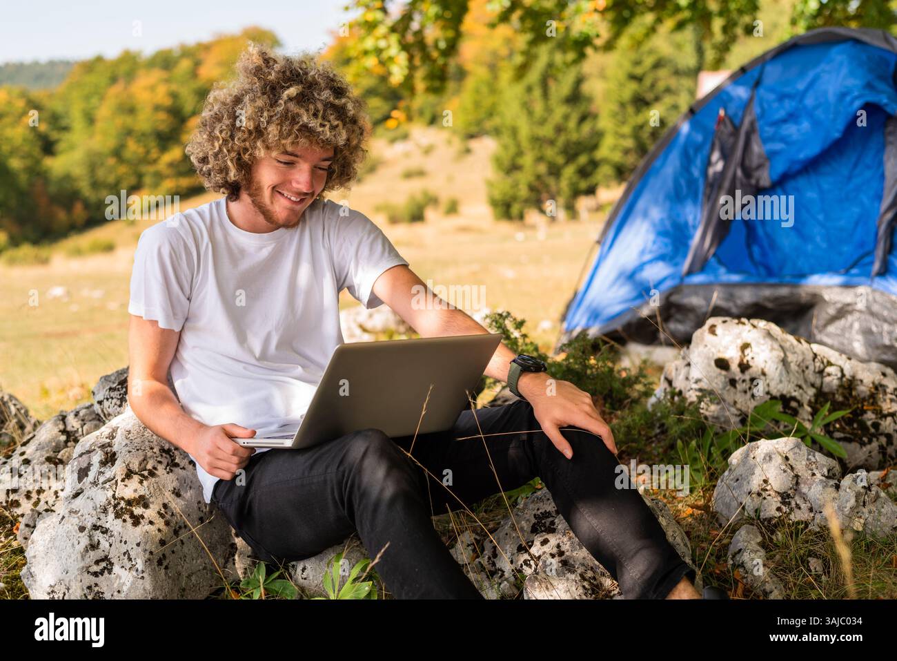 Young happy man freelancer working online using laptop in nature. Stock Photo
