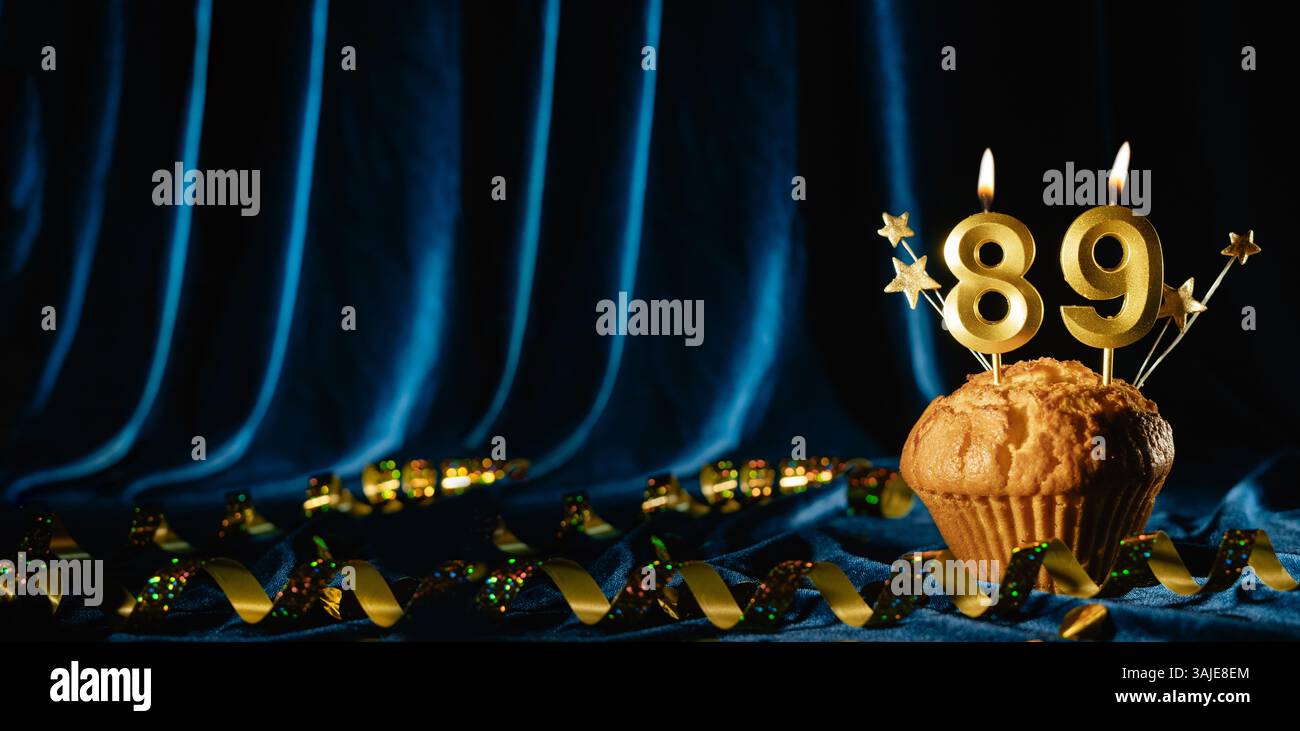 Number 89 gold celebration candle and small stars in sweet cupcake on bright blue velvet background. Concept of celebrating birthday, anniversary Stock Photo