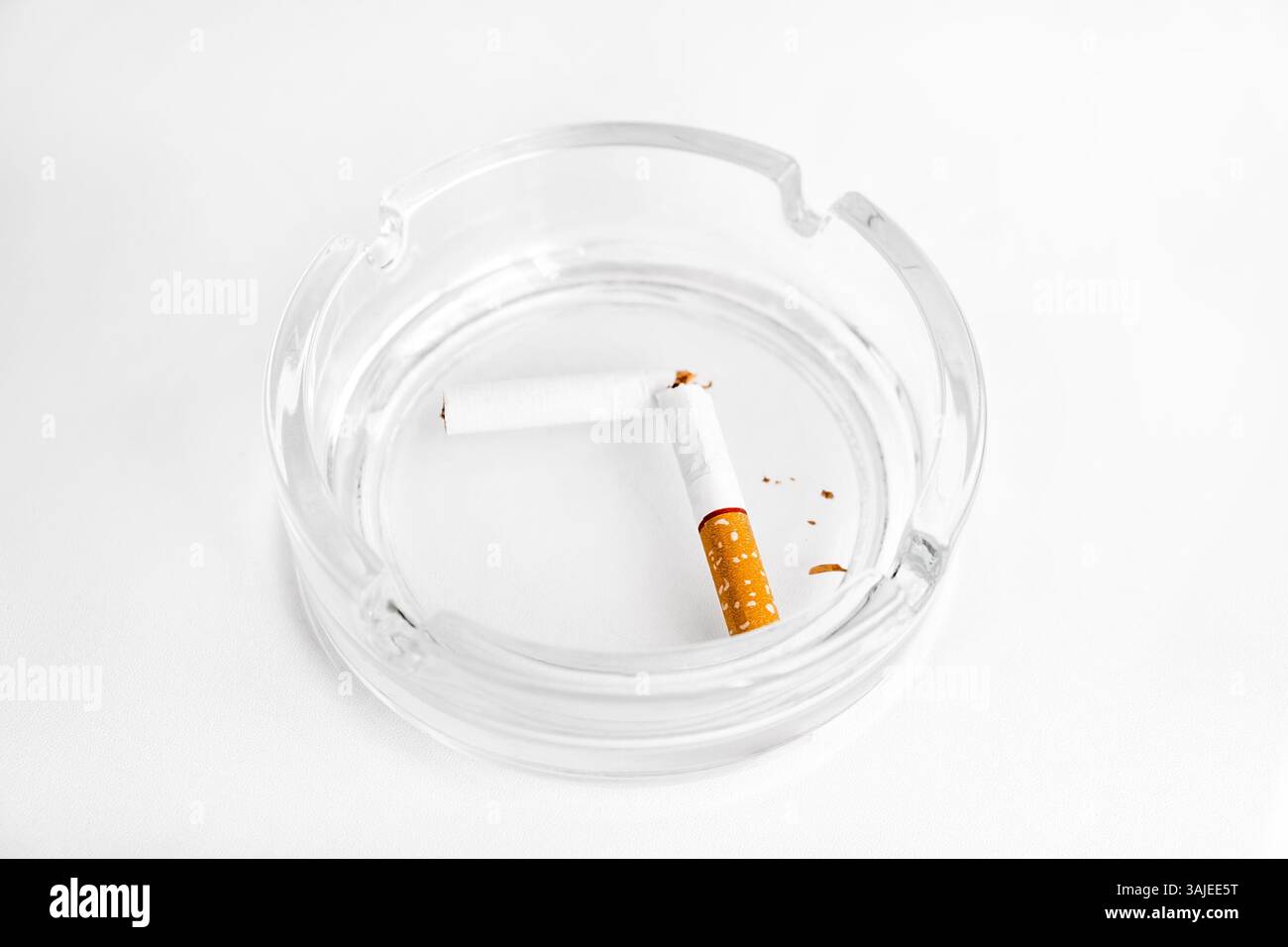 Broken Cigarette in Ashtray on the White Table Background closeup Stock Photo
