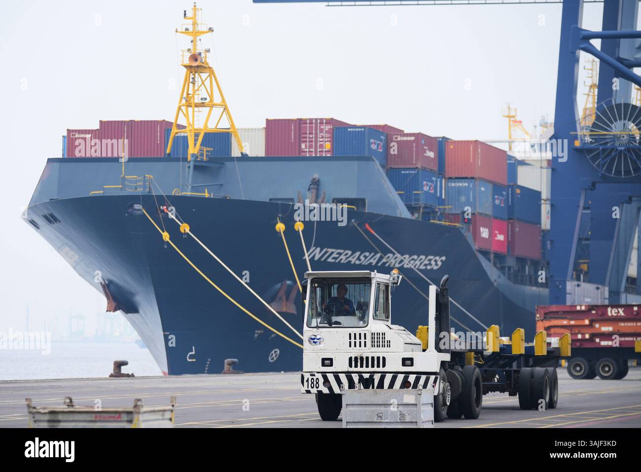 A truck drives past a cargo ship carrying containers at Jakarta ...