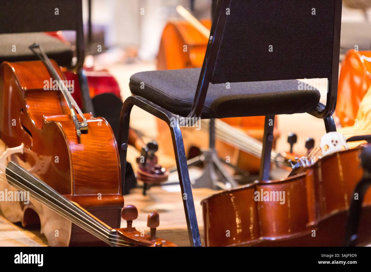 A chair sits among cellos and other stringed instruments, ready for the orchestra to play. Stock Photo