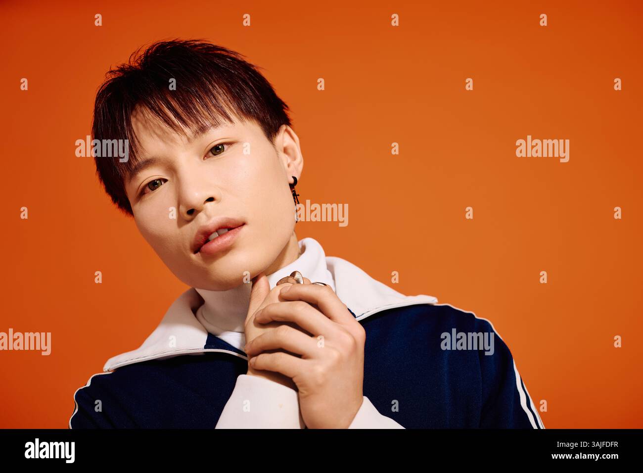 A stylish young man poses confidently against a vibrant orange ...