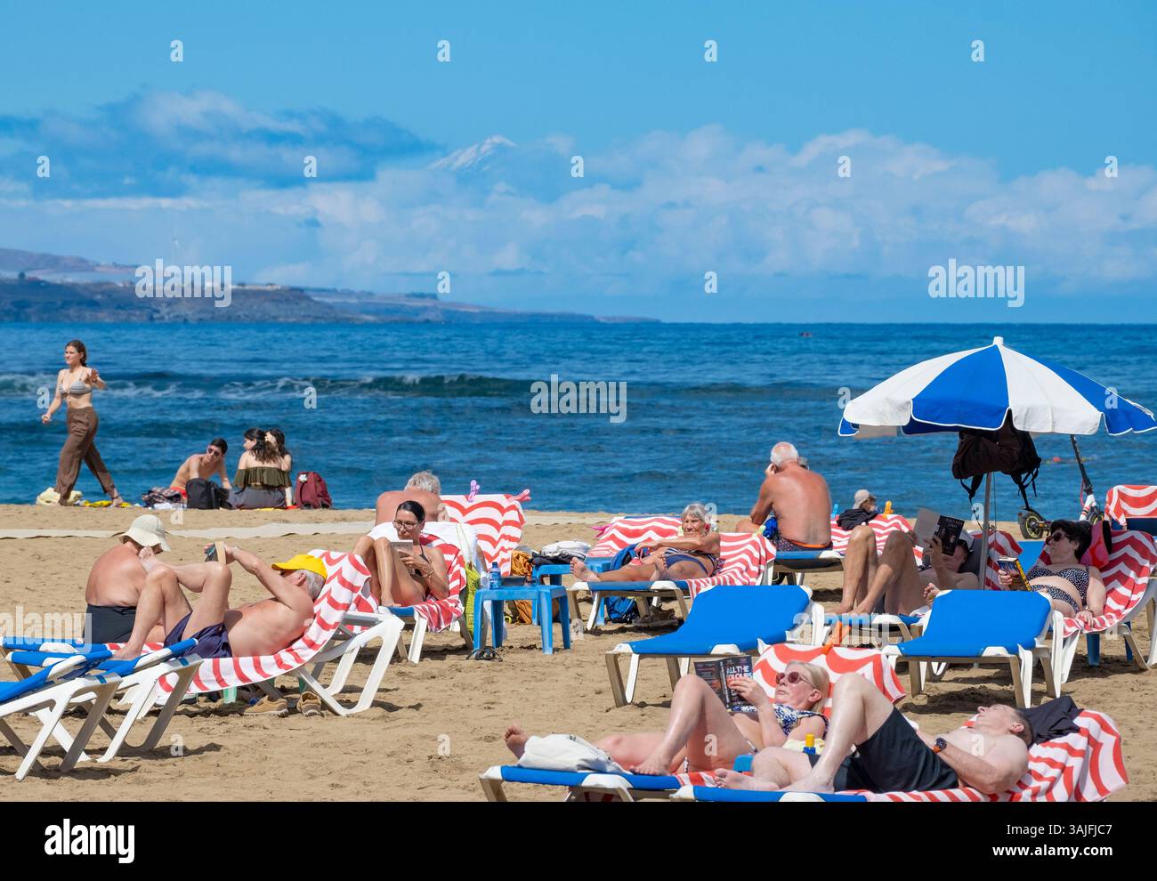 Las Palmas, Gran Canaria, Canary Islands, Spain. 11th April, 2025. Tourists, many British, sunbathe on the city beach in Las Palmas in the wake of storm Olivier. The storm covered Spain's highest mountain, mount Teide on Tenerife, in a blanket of snow. Mount Teide can be seen here in the distance as people bask in glorious sunshine. Credit: Alan Dawson/Alamy Live News Stock Photo