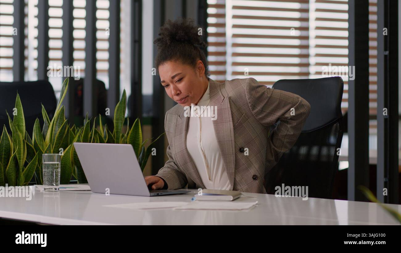 Sedentary work office African American woman girl businesswoman female business worker computer at desk feel pain suffer discomfort back ache health Stock Photo