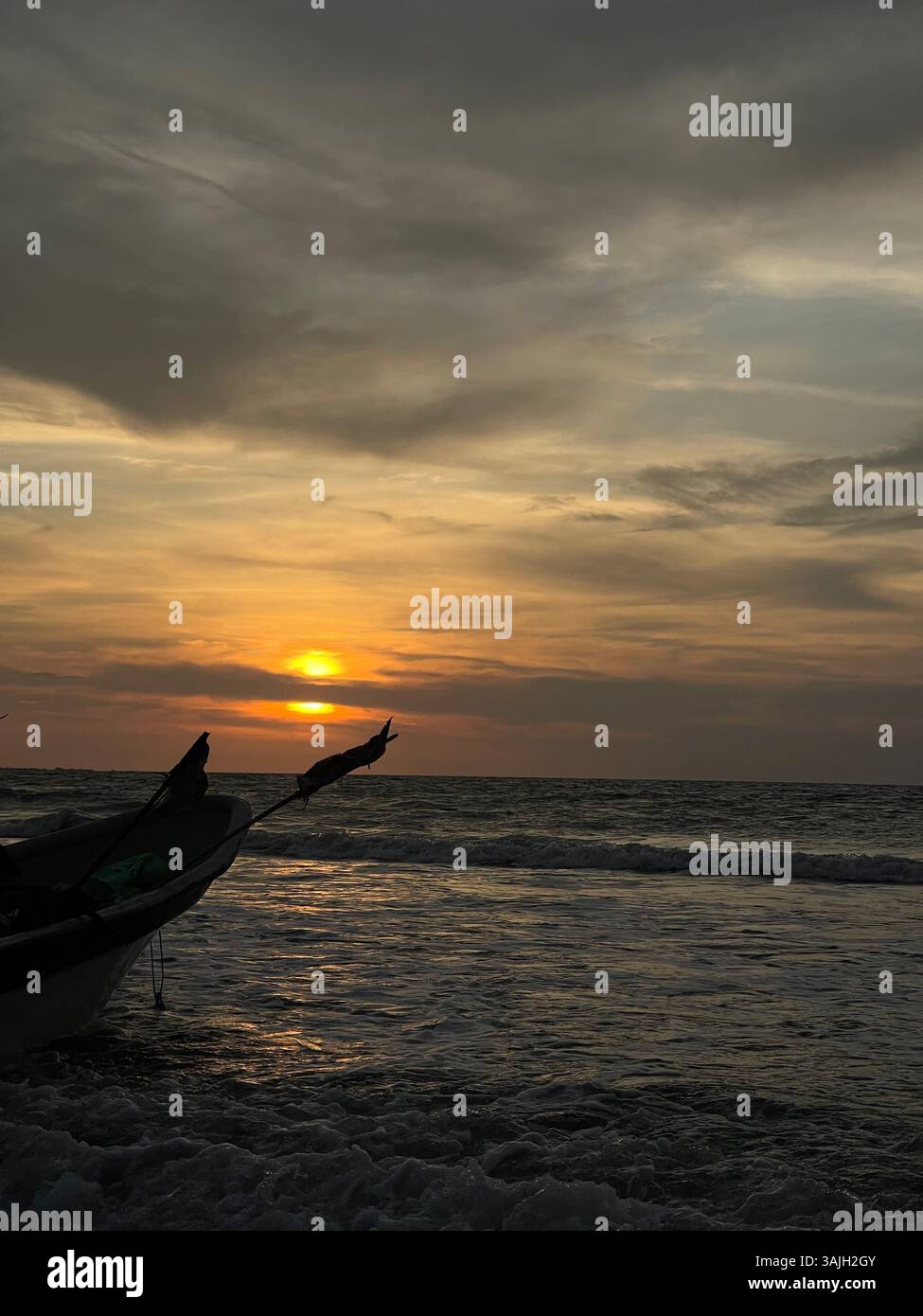 Traditional fishing boat silhouetted against a dramatic ocean sunset with golden skies. - Smartphone Captured Stock Image