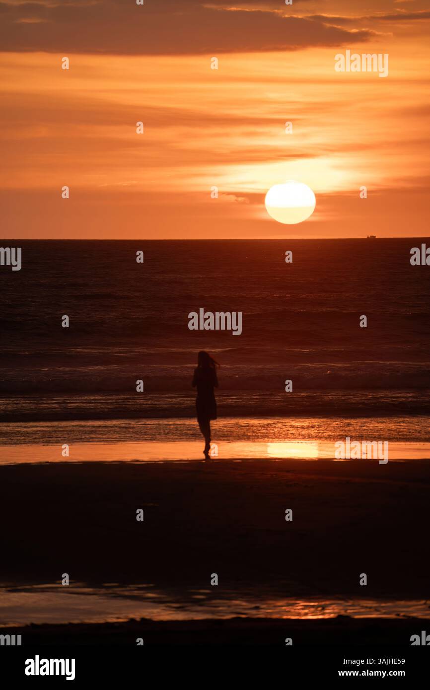 Solitary silhouette walking along Bali's shoreline at sunset, with ...