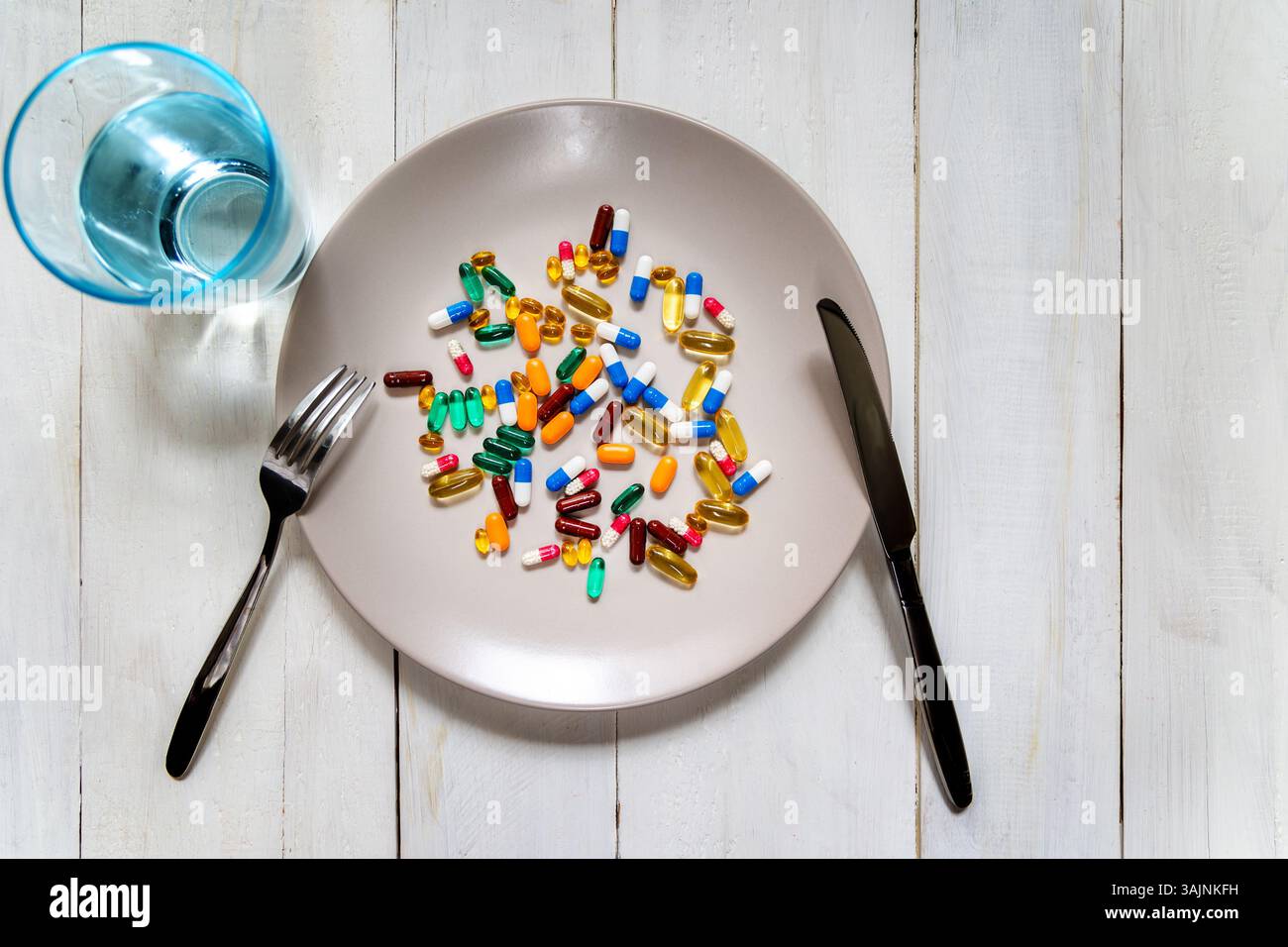 Mixed pills on plate with fork and knife. Various colorful capsules and tablets are scattered on a plate, styled like a meal, with cutlery and a glass Stock Photo