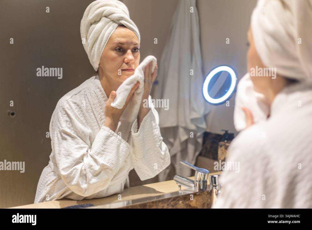 A woman applies a towel to her face as she focuses on her skincare routine in a well-lit spa environment, creating a calming and rejuvenating experien Stock Photo