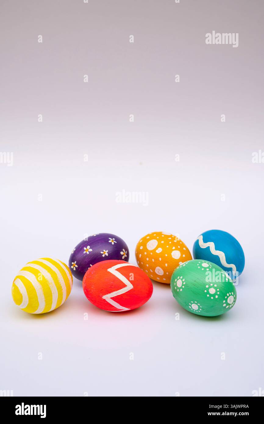 A creative Easter setup with hand-painted eggs in vivid colors and patterns arranged on a white studio backdrop. Stock Photo