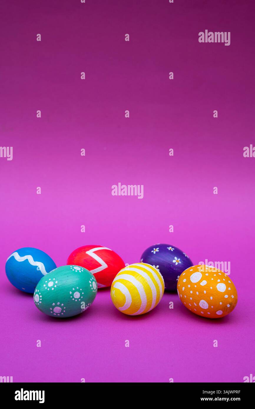 Vibrant Easter eggs decorated with different patterns, styled over a pastel pink surface for a festive vibe. Stock Photo