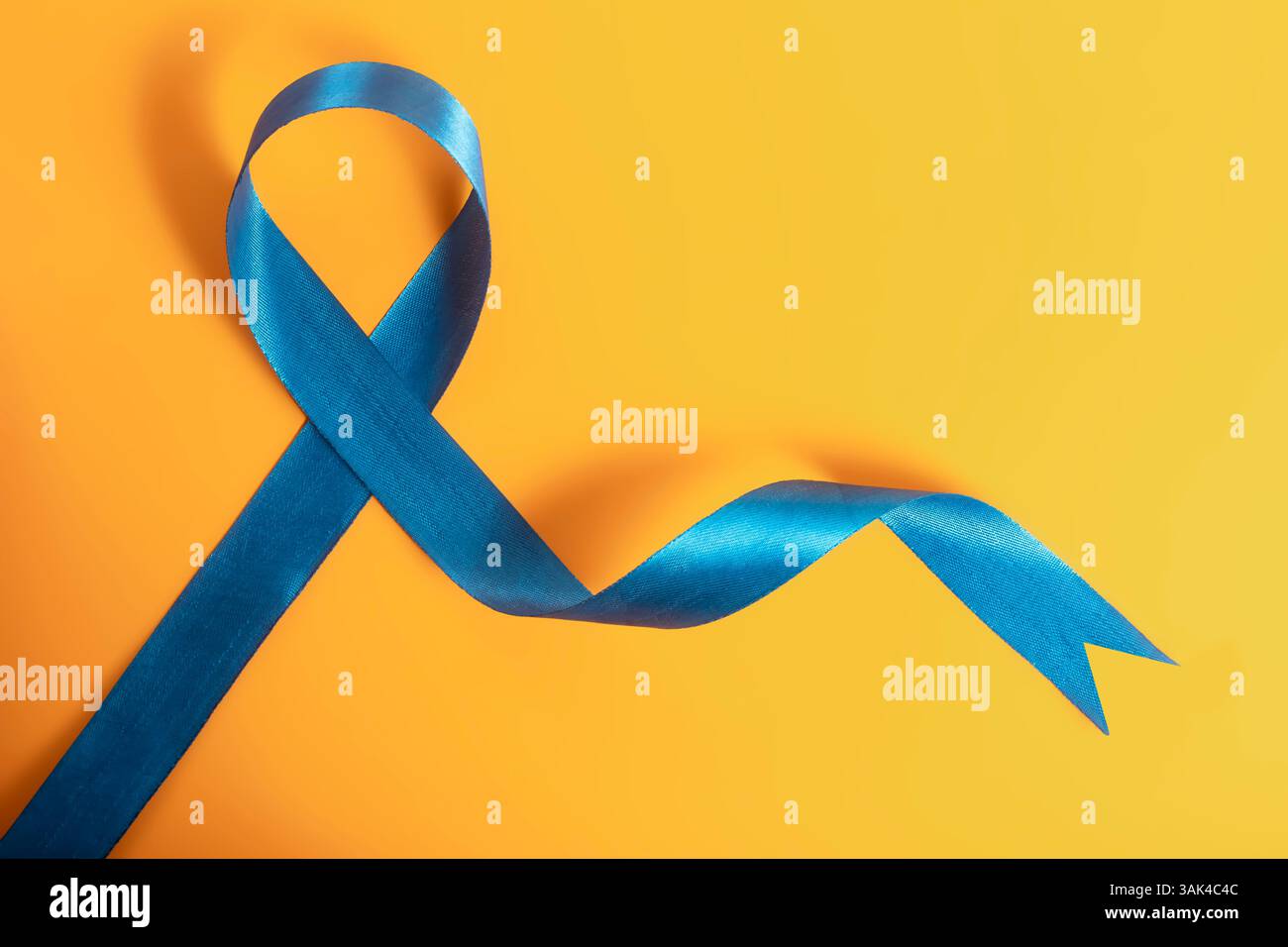 A bright blue awareness ribbon forms a loop on a contrasting yellow background, symbolizing cancer awareness, support campaigns, and support for vario Stock Photo