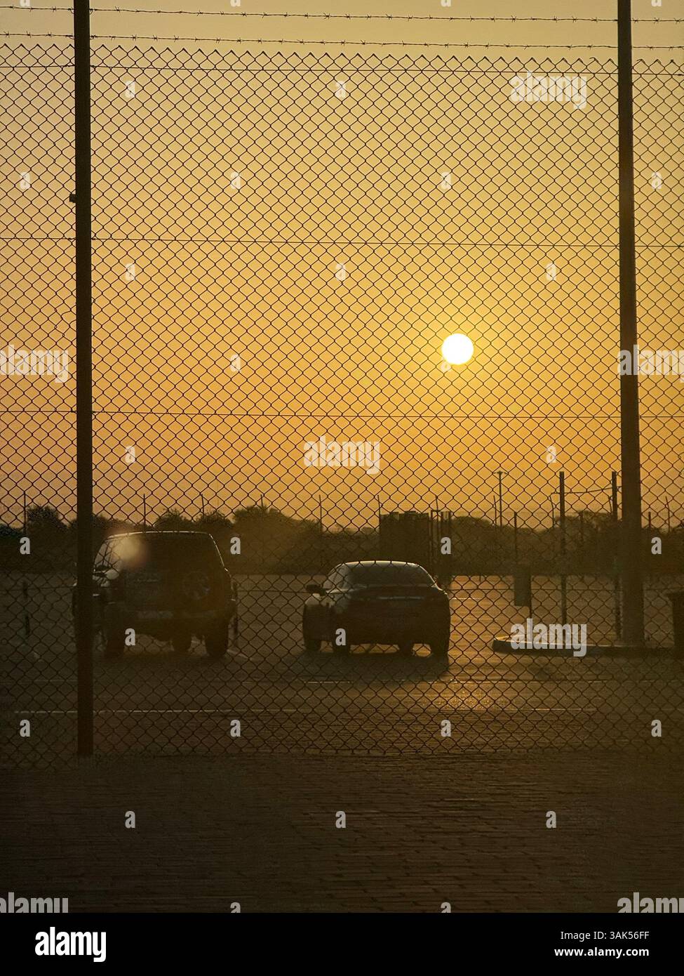 Sunrise at UAE–Oman border in Al Ain showing two cars through a fence, captured in HDR with iPhone. Orange sky and desert road at golden hour. - Smartphone Captured Stock Image