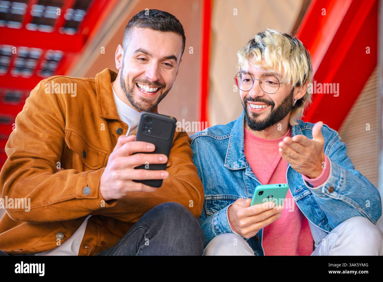 Friend Vs Screen Two friends laughing and pointing at smartphone screen in urban outdoor ...