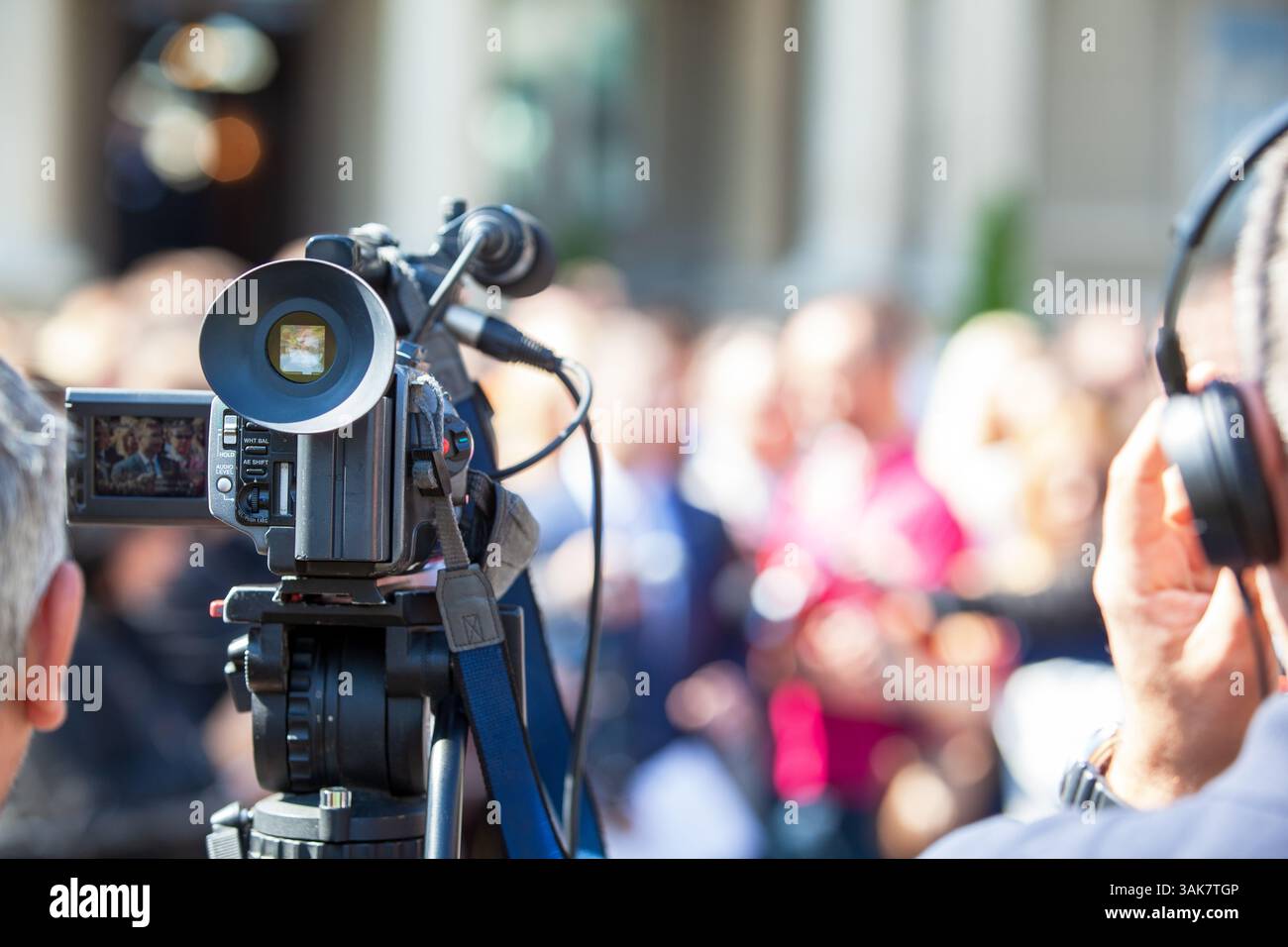Professional video camera capturing a live public event with a diverse ...