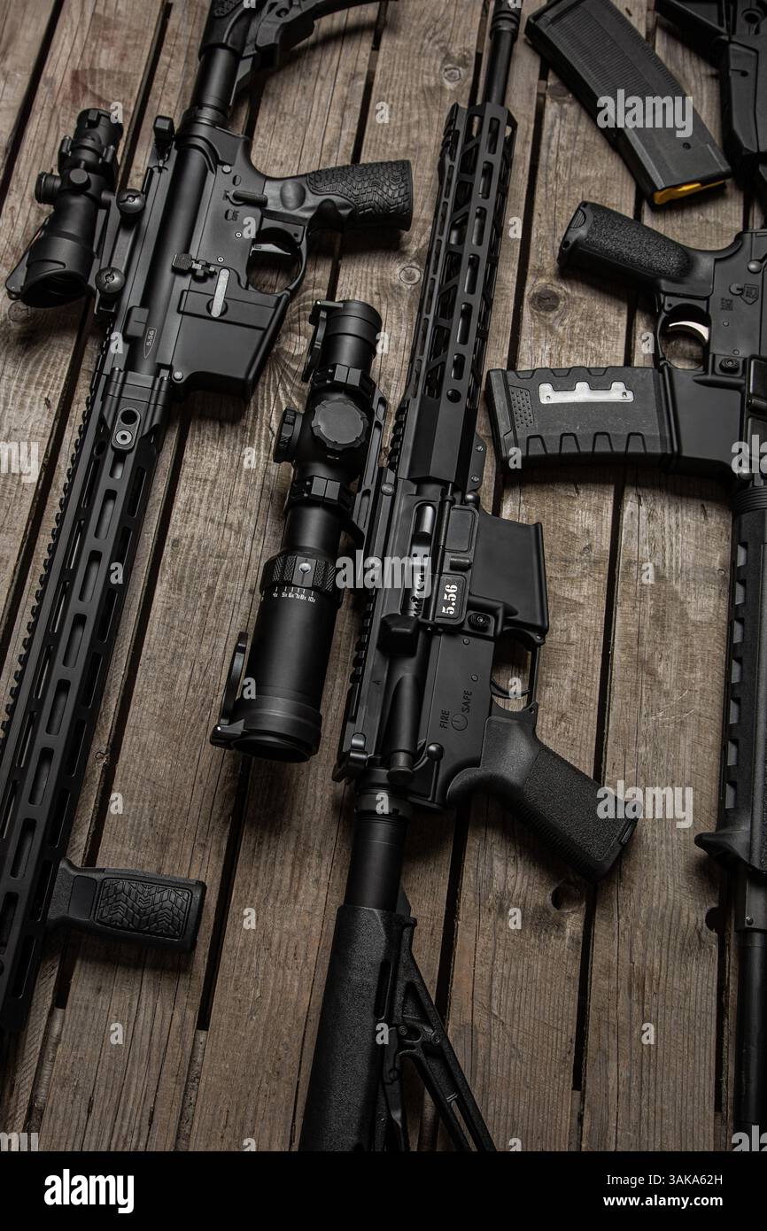 Multiple black tactical rifles and magazines laid out on wooden surface ...