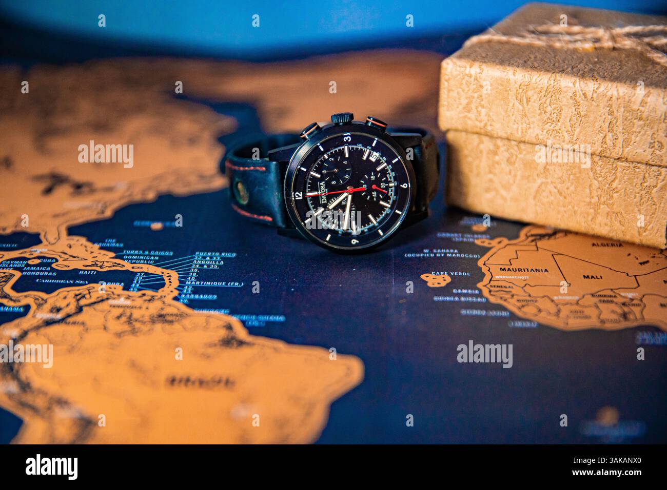 A black wristwatch placed on a travel map next to a piece of sandstone, symbolizing time and exploration Stock Photo