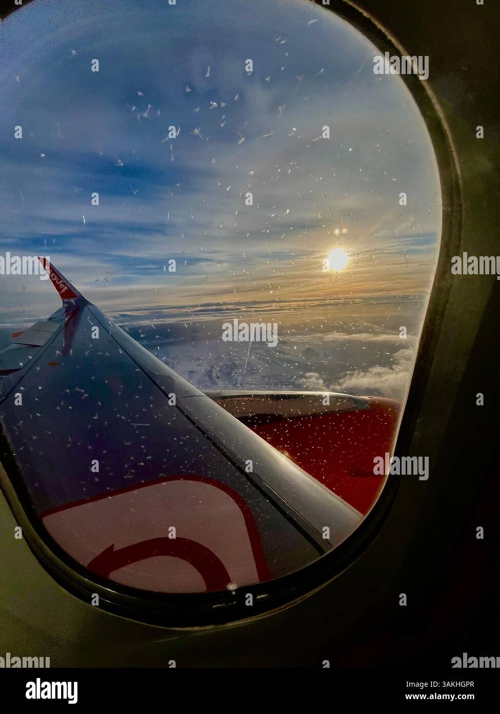 Setting sun on the horizon viewed from an aircraft window approaching Iceland with clouds and blue sky - Smartphone Captured Stock Image