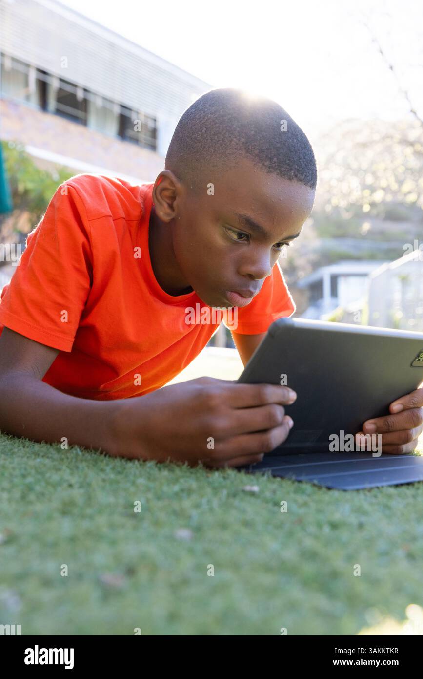 Lying on grass, boy using tablet for studying outside school building Stock Photo