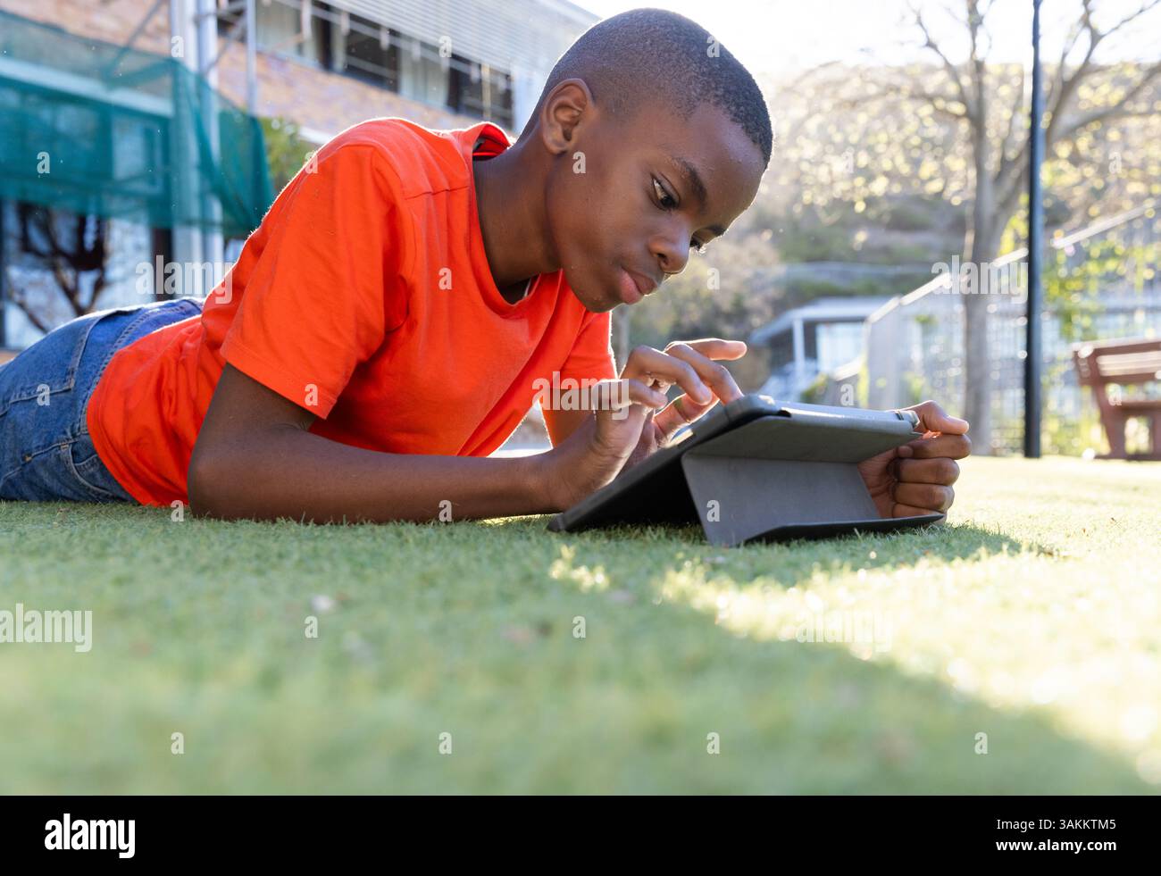 Using tablet, boy lying on grass in school, focusing on screen Stock Photo