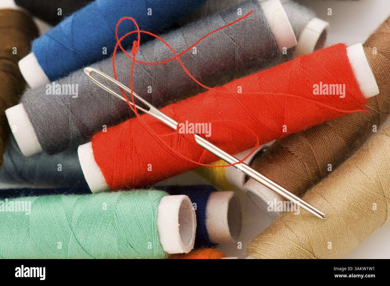 Many bobbins with different colored threads and needle Stock Photo