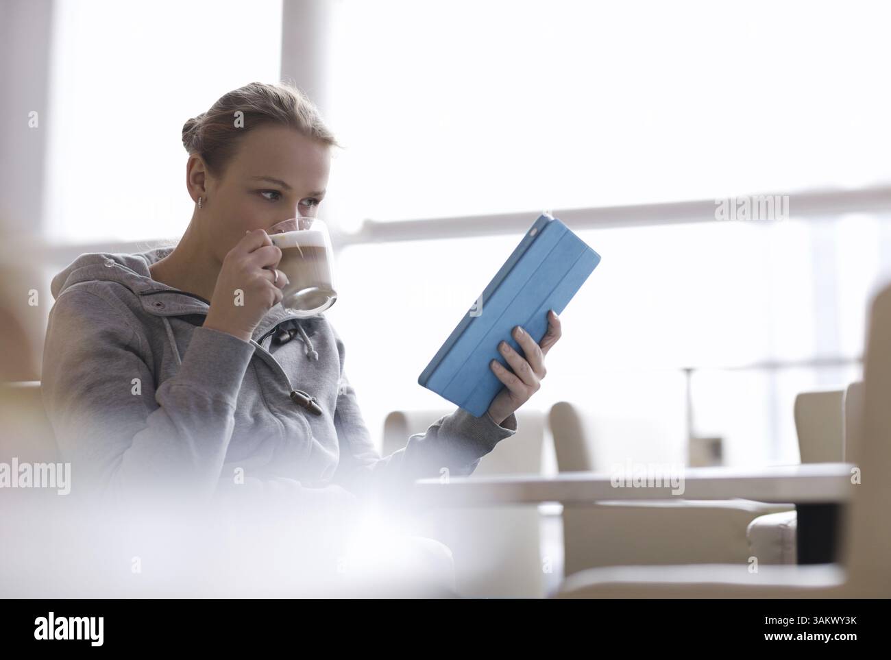 Young woman using her touchpad while drinking coffee in cafe Stock Photo