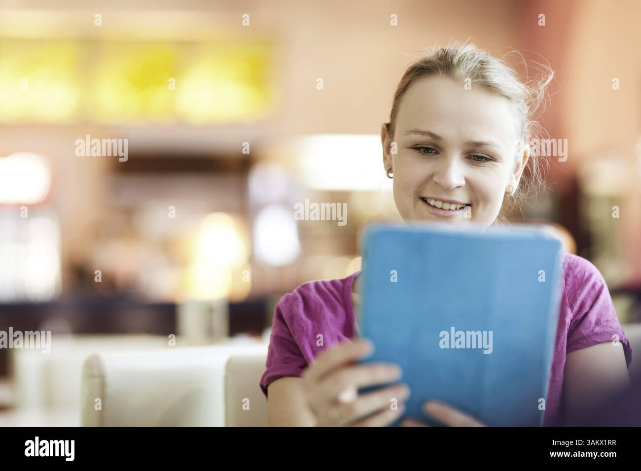 Young smiling woman in cafeteria using tablet computer Stock Photo