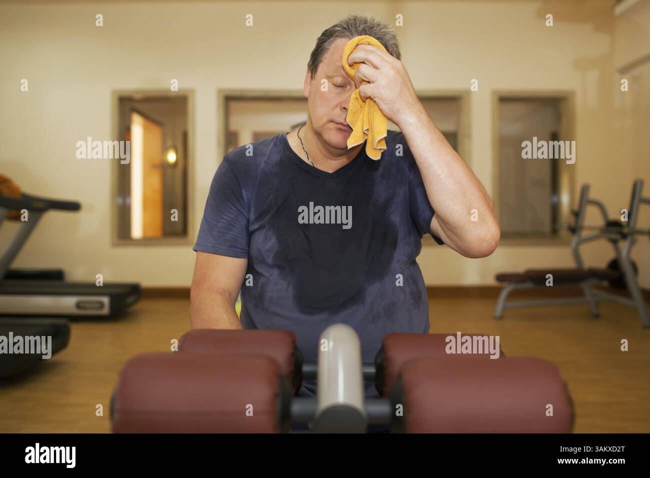 Exhausted mature man wiping sweat with a towel after intensive training in the gym Stock Photo