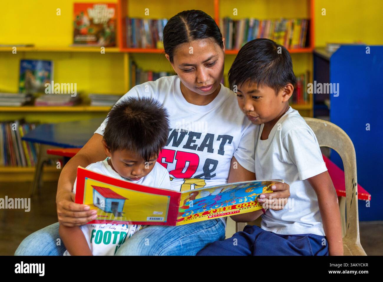 A Filipino mother reads with her two sons at a public elementary school library in Batangas, fostering early literacy and strong family bonds Stock Photo