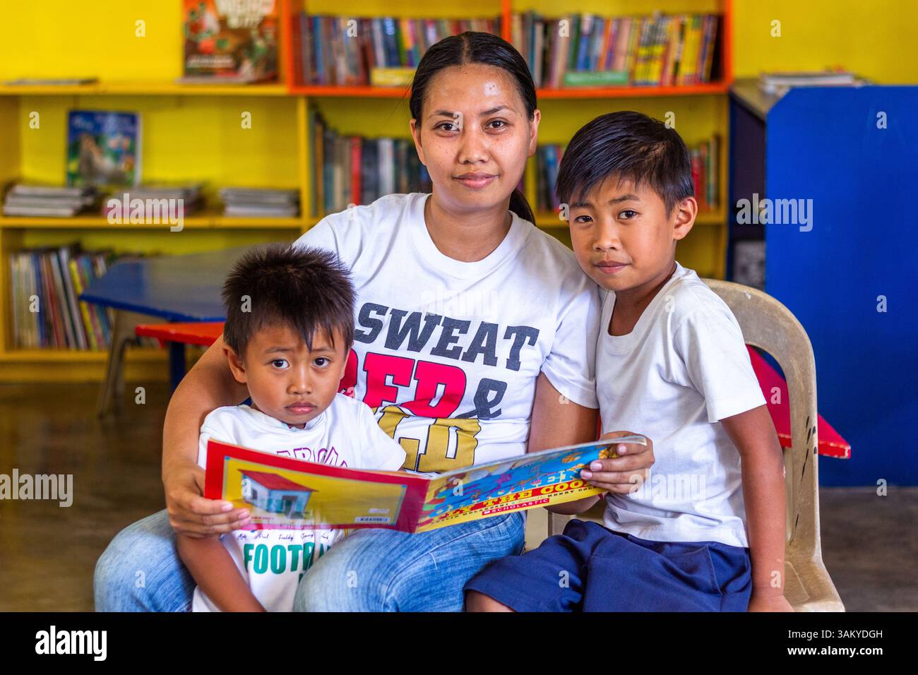 A Filipino mother reads with her two sons at a public elementary school library in Batangas, fostering early literacy and strong family bonds Stock Photo
