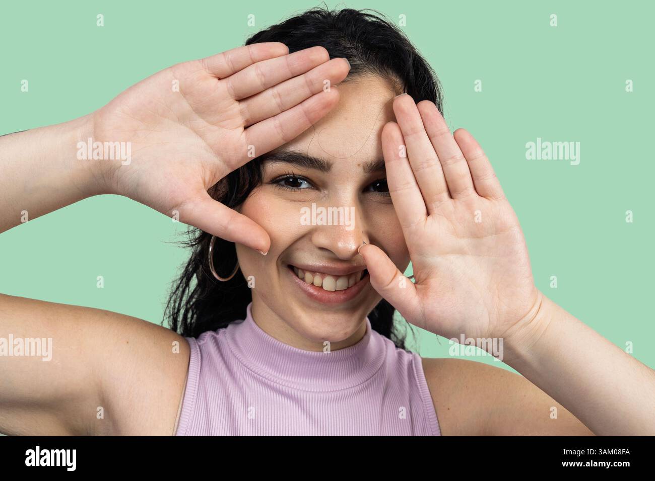 Cheerful young woman framing her face with hands and smiling on a green background Stock Photo