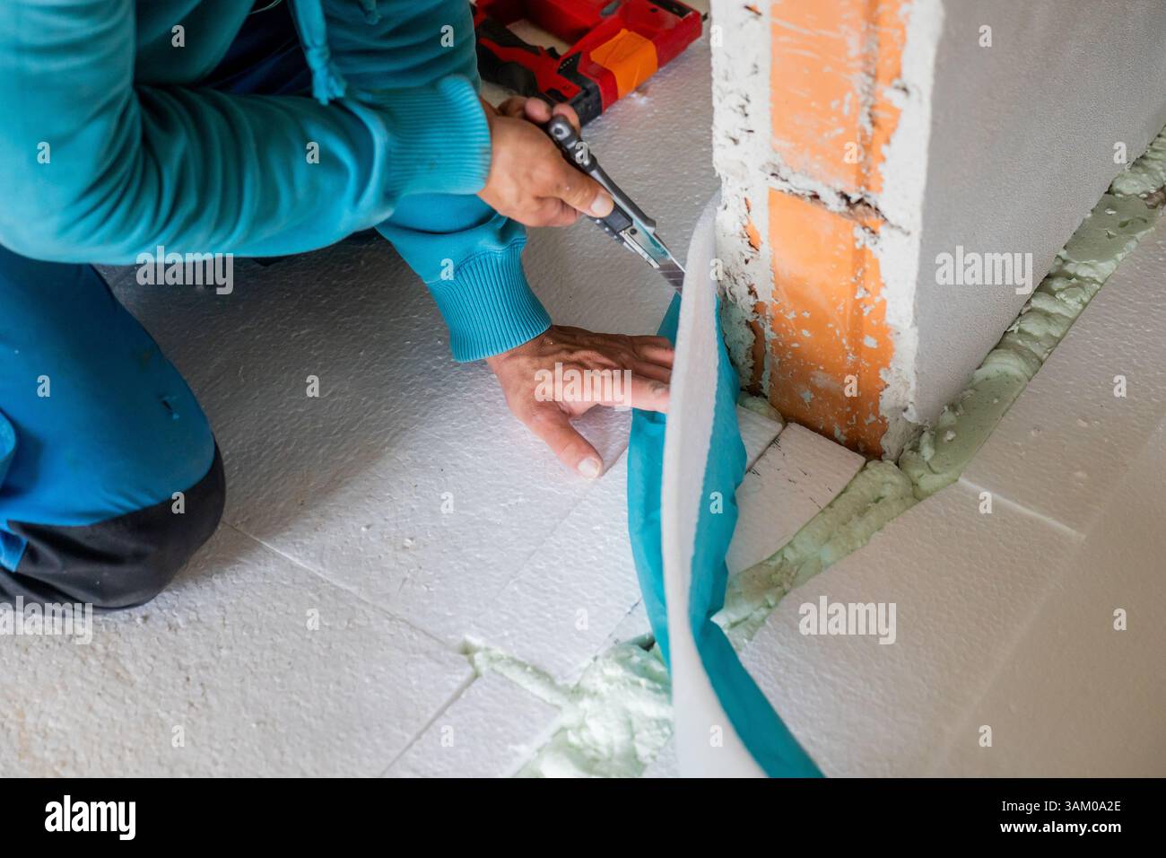 Construction worker is cutting edge insulation panel using utility knife during floor installation Stock Photo