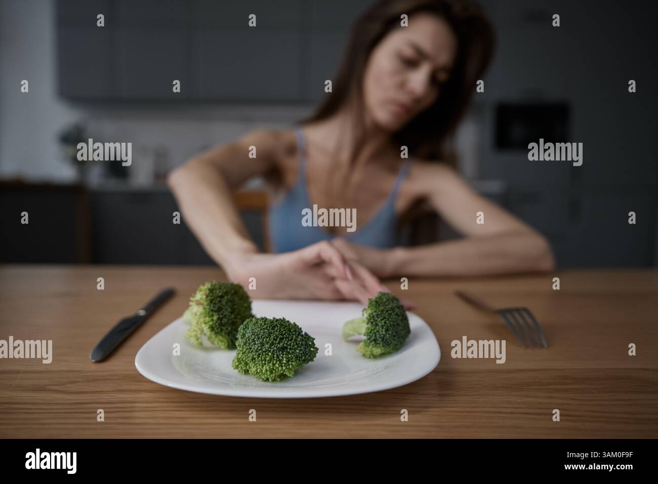 Skinny woman feeling nausea refusing to eat broccoli portion pushing plate away Stock Photo